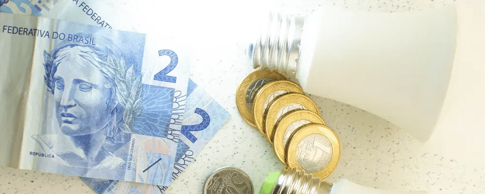 Notas de dois reais com moedas de um real e uma lâmpada de luz.